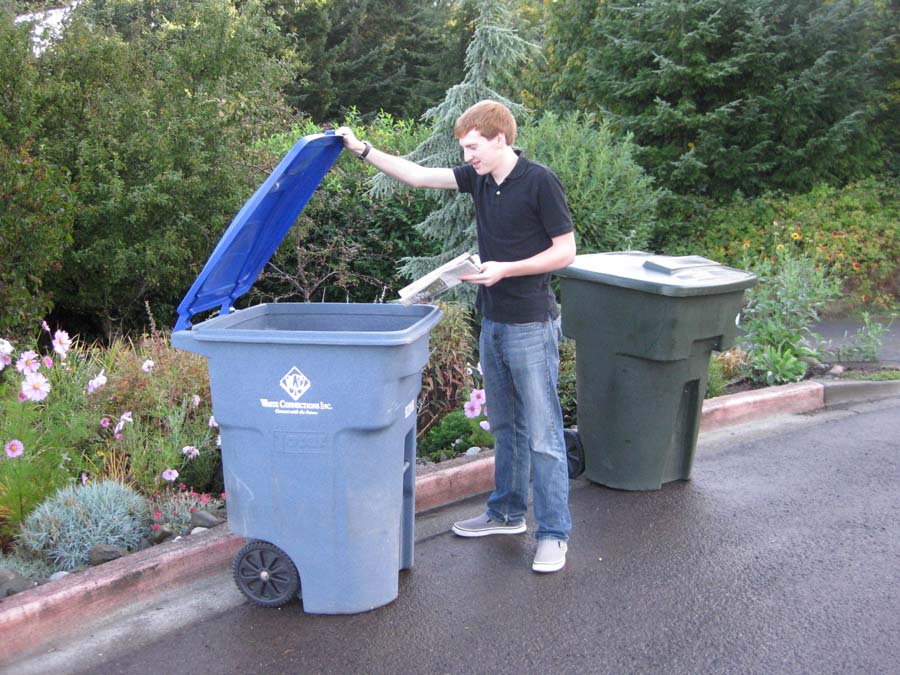 A young man putting recyclables into a blue recycling container.